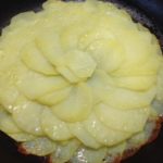 Patate finemente affettate, adagiate in padella per la preparazione della ricetta interamente vegetale di patate e cipolle in padella