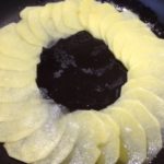Patate finemente affettate, adagiate in padella come primo strato nella preparazione della ricetta interamente vegetale di patate e cipolle in padella