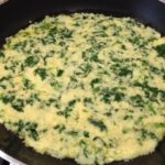 Purea di patate crude con erbette o spinaci ben distribuita nella padella con l'aglio e olio per la nostra gustosissima frittata senza uova! Comincia a prendere forma...